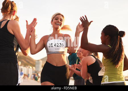 Multi ethnic group of young adults cheering and high fiving a female athlete crossing finish line. Sportswoman giving high five Stock Photo