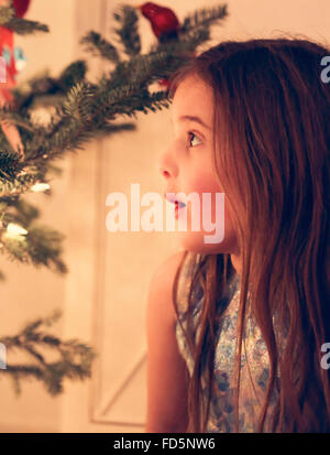 Profile of a little girl staring at a glowing Christmas tree with a look of wonder on her face.