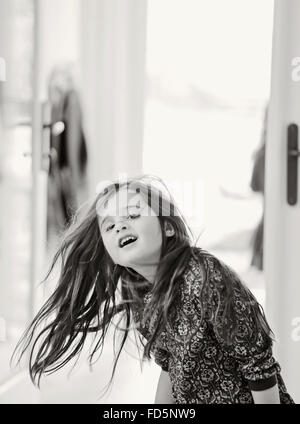 Black and white image of a young girl dancing and playing, swinging her long, brown hair and smiling. Stock Photo