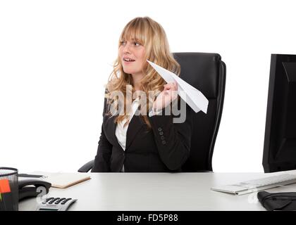 Mischievous businesswoman with a paper plane taking aim at a colleague as she sits at her desk Stock Photo