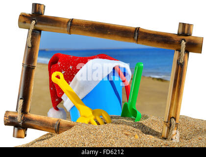 Baby toys and Santa's hat  in bamboo frame on the beach against a blue ocean isolated on white background Stock Photo