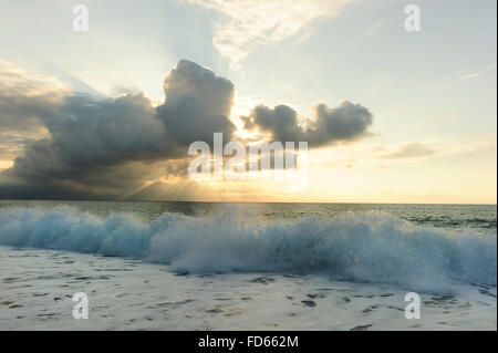 Ocean waves is brightly light golden seascape with waves rolling to the shore as scattered sunbeam break through a dramatically