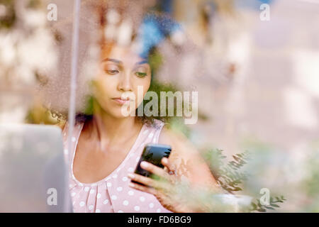 Woman using her phone seen through the window of cafe Stock Photo