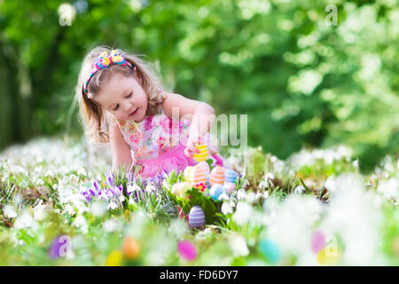Little girl having fun on Easter egg hunt. Kids in blooming spring garden with crocus and snowdrop flowers. Stock Photo