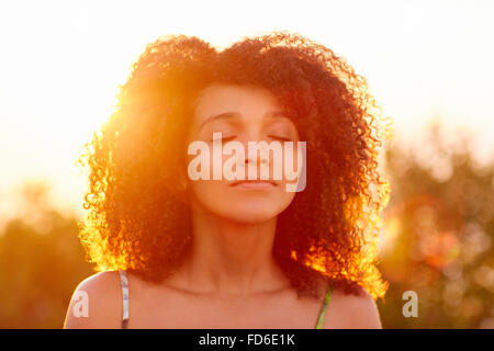 Curly hair woman closing her eyes on summer evening Stock Photo