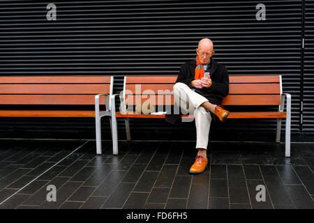 A mature man using mobile while sitting on public bench, London Stock Photo