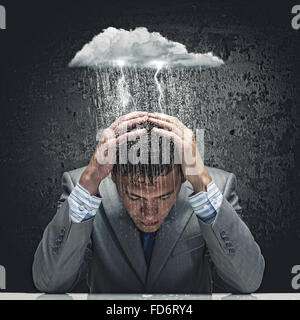 Depressed young businessman sitting wet under rain Stock Photo