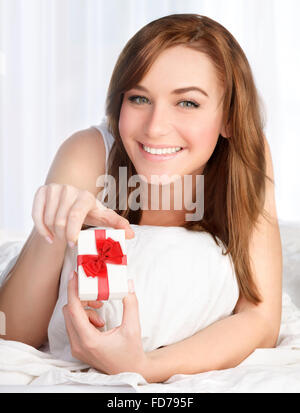 Portrait of beautiful woman lying down in the bed at home with little gift box in hands, happy morning of Valentine day Stock Photo