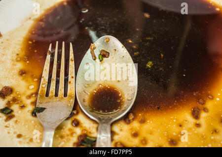 Dirty and empty finished plate with fork and spoon to be cleansed Stock Photo