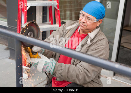 Construction worker cutting steel pipe with angle grinder tool - USA Stock Photo