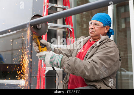Construction worker cutting steel pipe with angle grinder tool - USA Stock Photo