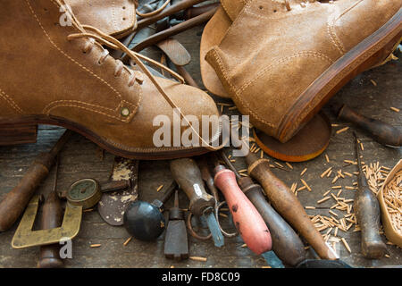 Old shoemaker tools with handmade shoes on workshop bench. Stock Photo