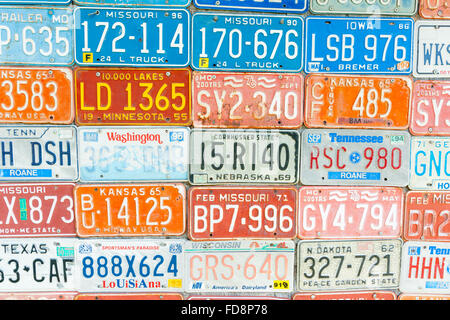 Old out of date Vehicle registration plates mounted on wall showing range of colors, states, numbers and state nick names. Stock Photo