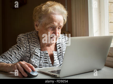 An elderly woman sitting at the table and types on laptop.