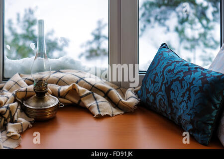 Beige woolen scarf and old lamp located on stylized wooden window sill. Winter concept of comfort and relaxation. Stock Photo