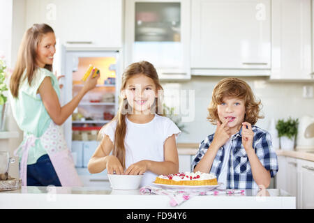 Mother and two children baking and tasting a fruit cake in the kitchen Stock Photo