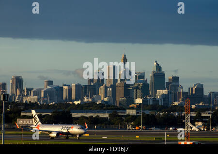 Jetstar aircraft landing at Kingsford-Smith airport, CBD tower buildings in distnace, Sydney, New South Wales, Australia Stock Photo