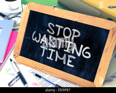Stop Wasting Time - Chalkboard with Hand Drawn Text, Stack of Office Folders, Stationery, Reports on Blurred Background. Toned I Stock Photo
