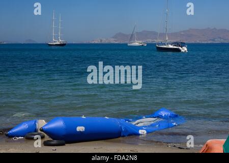 Collapsed inflatable dinghy used by migrants to reach Greece from Turkey on the beach at Kos Town with Turkey visible beyond. Stock Photo