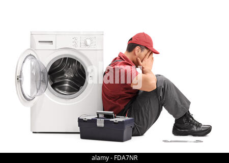 Studio shot of a disappointed young repairman sitting by a broken washing machine isolated on white background Stock Photo