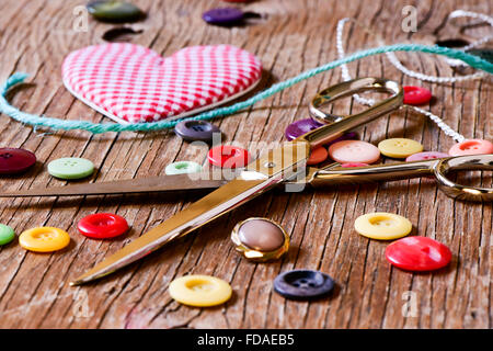 a heart made with a red and white checkered fabric, a pair of scissors, string and many buttons of different colors, on a rustic Stock Photo