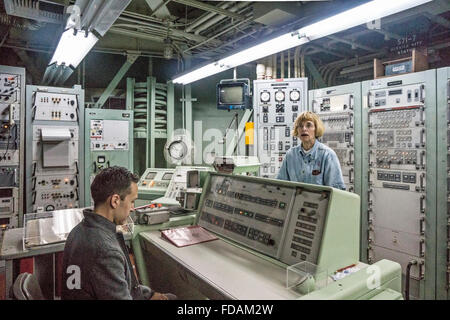 interior launch control room as tour leader describes process & serious young visitor sits at launch console to assist in launch Stock Photo