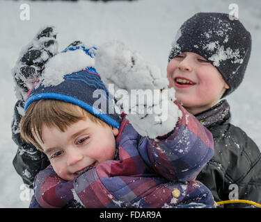 A big brother pulls off his little brother's hat after sliding down a snow covered hill.  The boys are smiling &covered in snow. Stock Photo