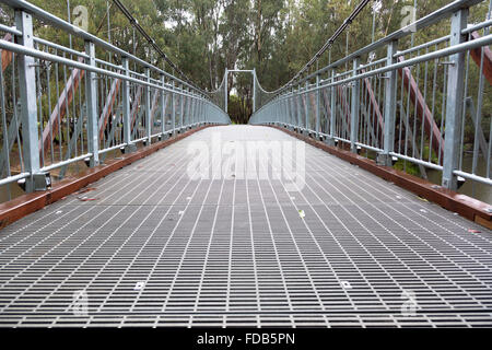 A large steel suspension foot bridge over a river nestled in the Australian bush. Stock Photo