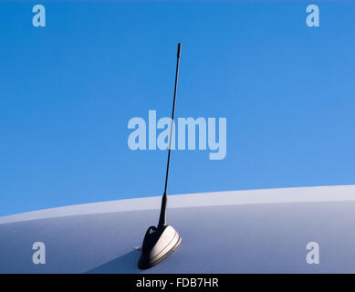 Short black antenna attached to smooth curved gray surface against clear blue sky. Stock Photo