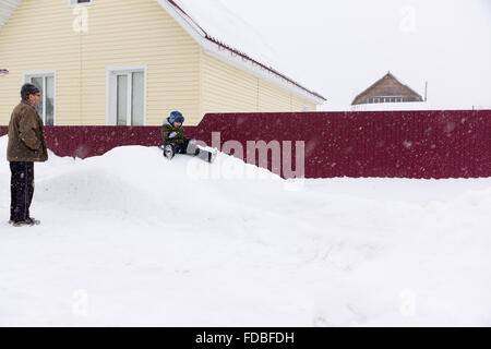 a little boy riding on a snowy hill in the care of grandparents Stock Photo