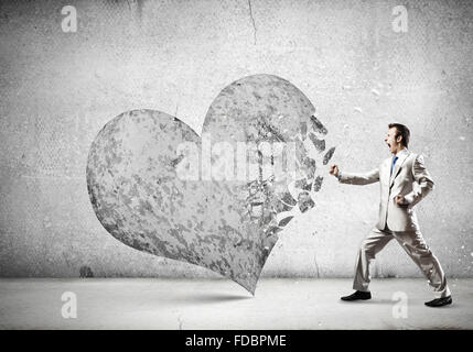 Young businessman breaking stone heart with punch Stock Photo