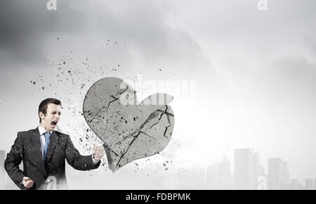 Young businessman breaking stone heart with punch Stock Photo