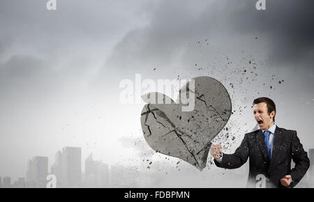 Young businessman breaking stone heart with punch Stock Photo