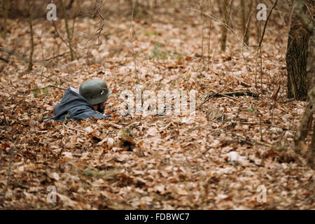 Hidden unidentified re-enactor dressed as german wehrmacht soldier aiming a rifle at enemy from ground Stock Photo