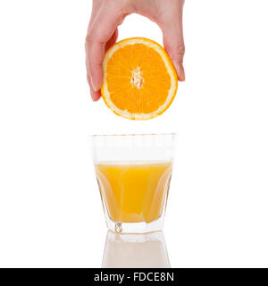 Freshly squeezed orange juice. Female hand squeezing orange into a glass isolated on white background. Healthy juice drink. Stock Photo