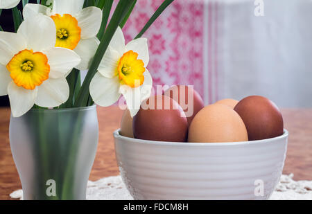 On the table on a lace napkin stands a vase with Easter eggs. Next to him a large white daffodils. Presented on the background o Stock Photo