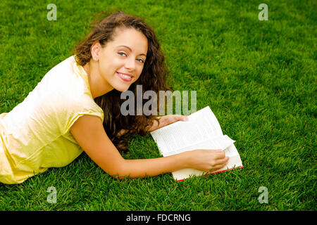 Beautiful young woman lying on the grass and reading a book Stock Photo