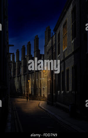 Night street scene in Cambridge showing row of chimneys with two people walking under the lamp light  United Kingdom Stock Photo