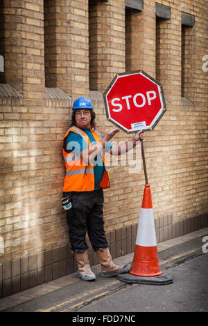 Workman in the street holding a stop sign with a blue helmet and an orange jacket. Stock Photo