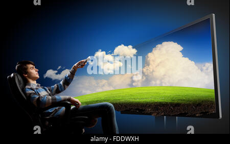 Young man in armchair with click watching TV Stock Photo