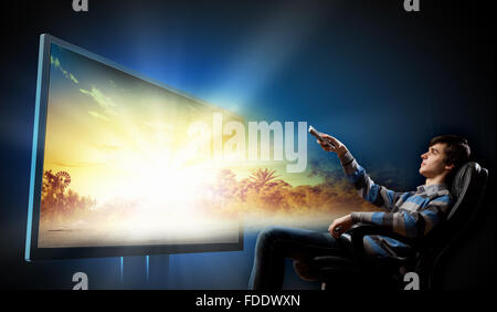 Young man in armchair with click watching TV Stock Photo