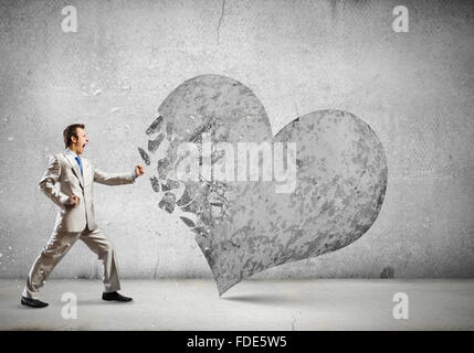 Young businessman breaking stone heart with punch Stock Photo