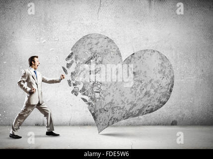 Young businessman breaking stone heart with punch Stock Photo