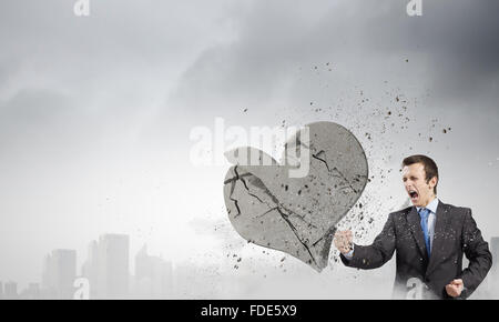 Young businessman breaking stone heart with punch Stock Photo