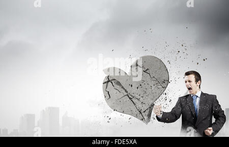 Young businessman breaking stone heart with punch Stock Photo