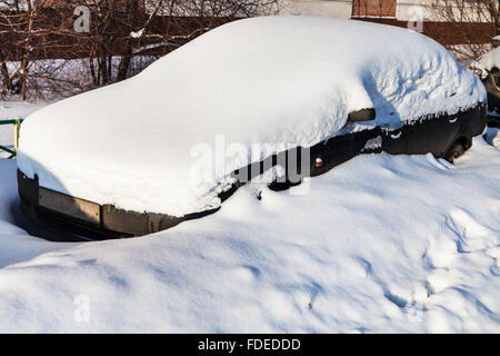 black car under fresh snow in parking lot near city house Stock Photo