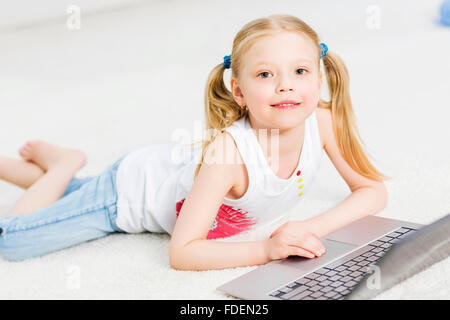 Cute girl laying on the floor and play at laptop Stock Photo