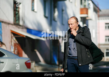 Brutal street photographer with camera in hand strolling city streets, talking on a walkie-talkie handsfree. Stock Photo