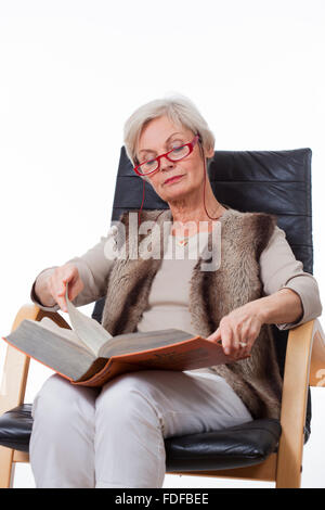 smiling senior old woman reading book in chair Stock Photo