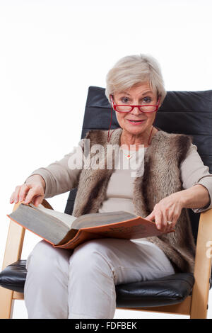 smiling senior old woman reading book in chair Stock Photo